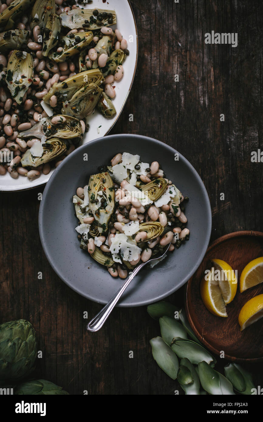 A bowl of braised baby artichoke salad with white beans and shaved manchego is photographed from the top. Stock Photo