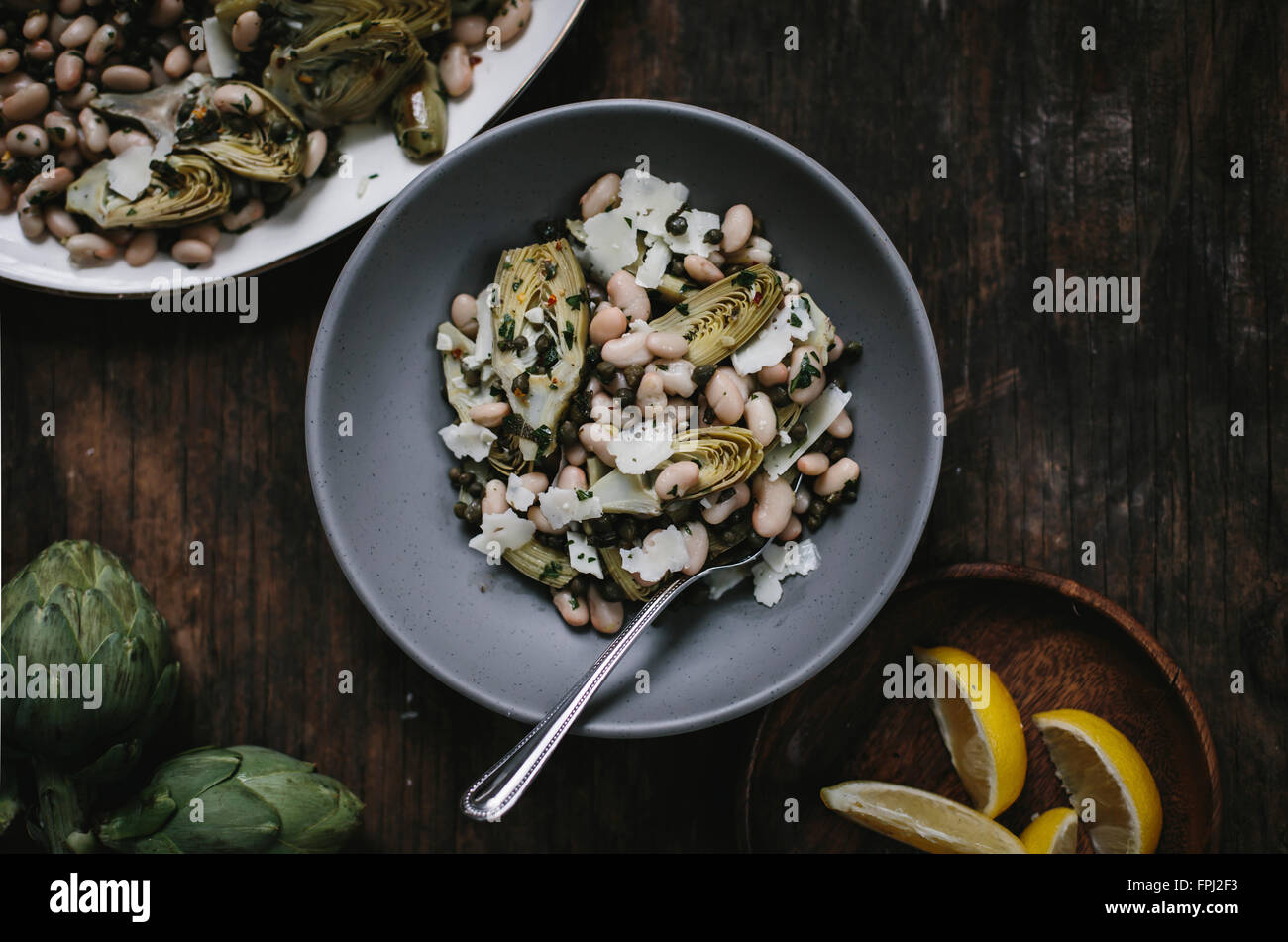 A bowl of braised baby artichoke salad with white beans and shaved manchego is photographed from the top. Stock Photo