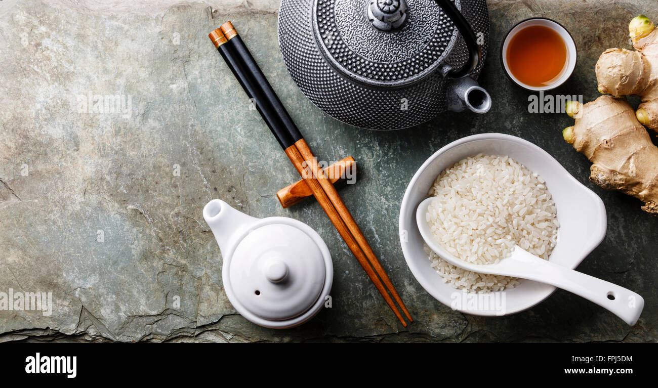 Raw white rice, green tea teapot, soy sauce and sushi chopsticks on gray stone slate background Stock Photo