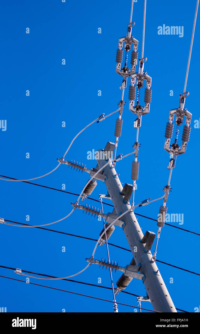 Right-angle junction of electrical power lines and insulators on pole against clear blue sky. Stock Photo