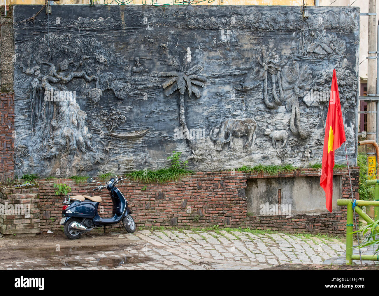 Hoi An, Vietnam, street scene with scooter, Vietnamese flag and a mural showing a country scene and seascape Stock Photo
