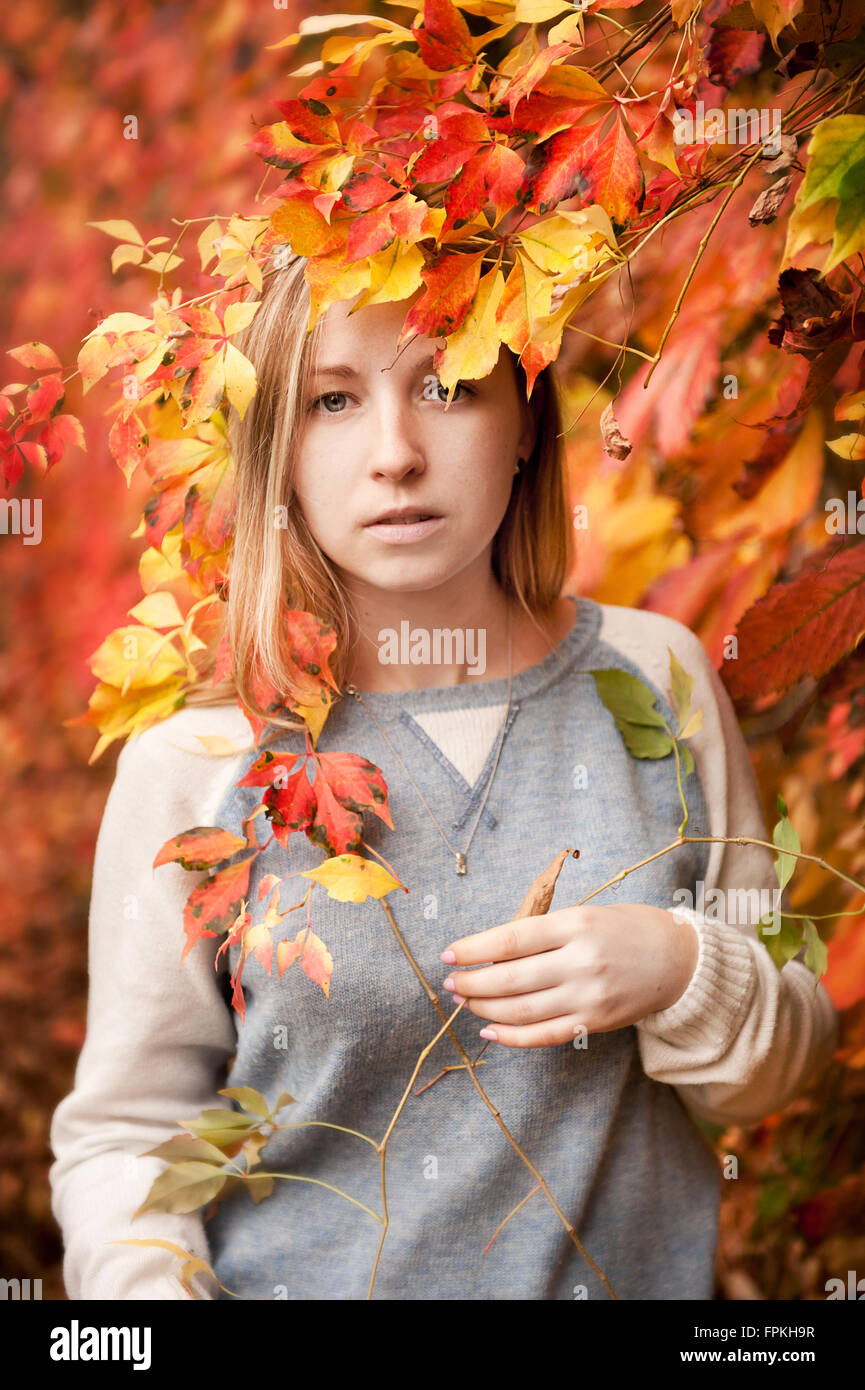 Autumn girl portrait in red yellow ivy leaves in vertical orientation, young blond hair girl in grey sweater, autumn nature Stock Photo
