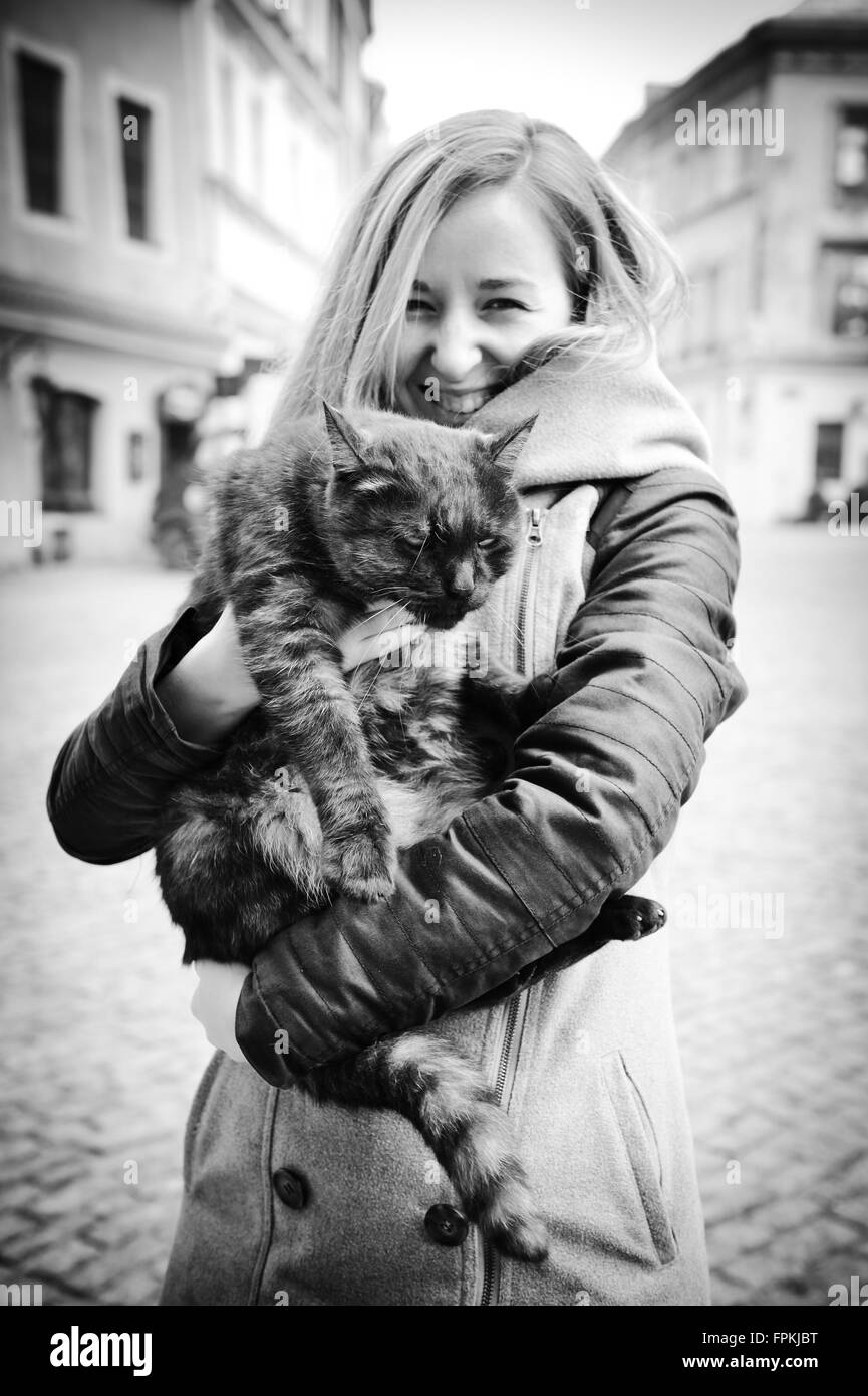 Woman holding unhappy cat, young female smiling happily and holding animal in arms and the angry cat wants to go back down Stock Photo