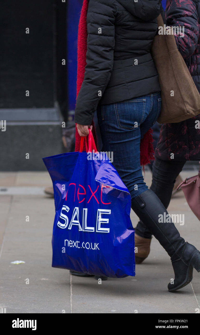 Woman carrying goods, half price items in a blue shopping bag,  purchased from Next clothing shop; Sale Event in Chester, Cheshire, UK 19th March, 2016. Stock Photo