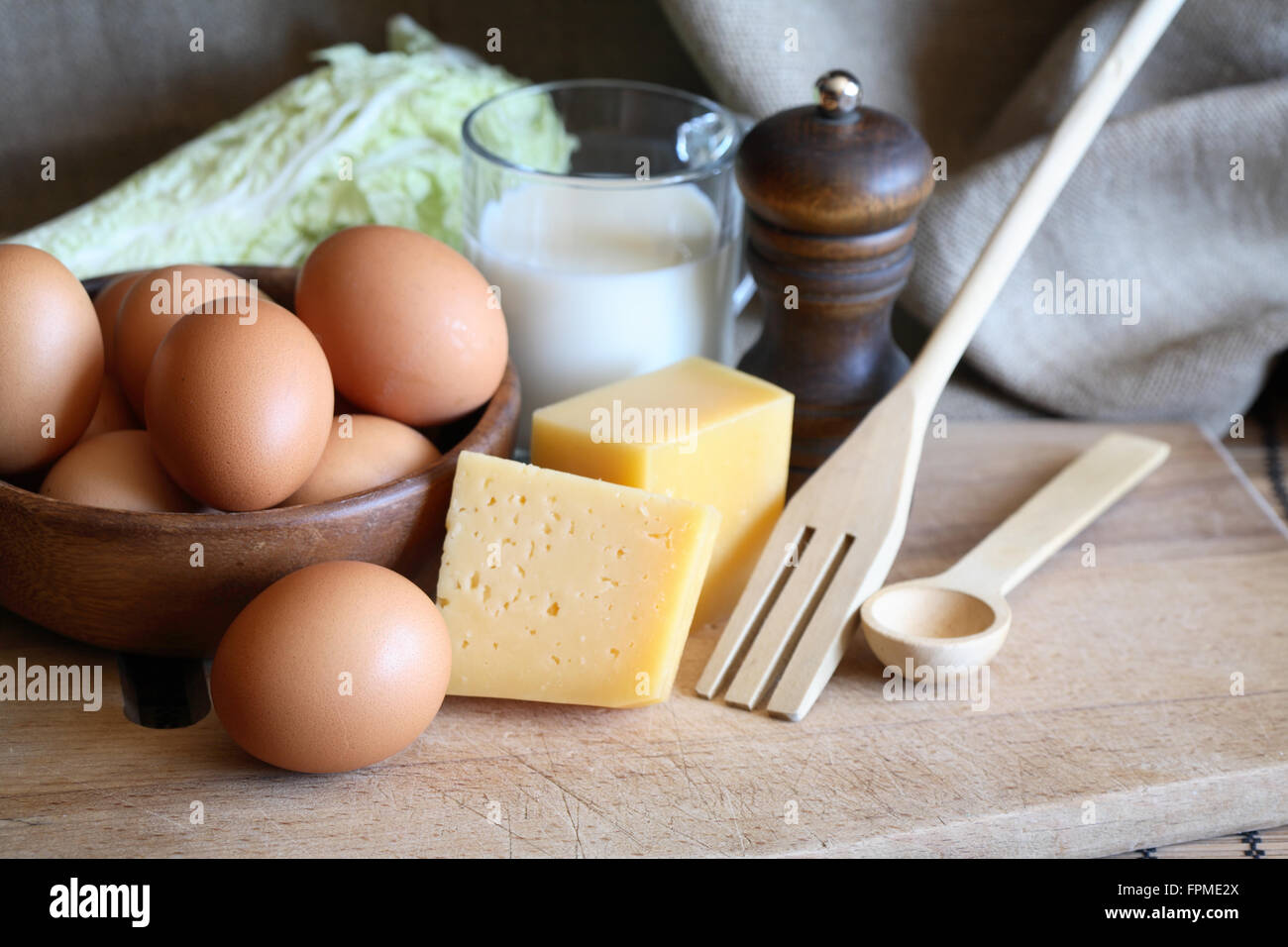 Bowl with raw eggs near cheese on wooden cutting board Stock Photo