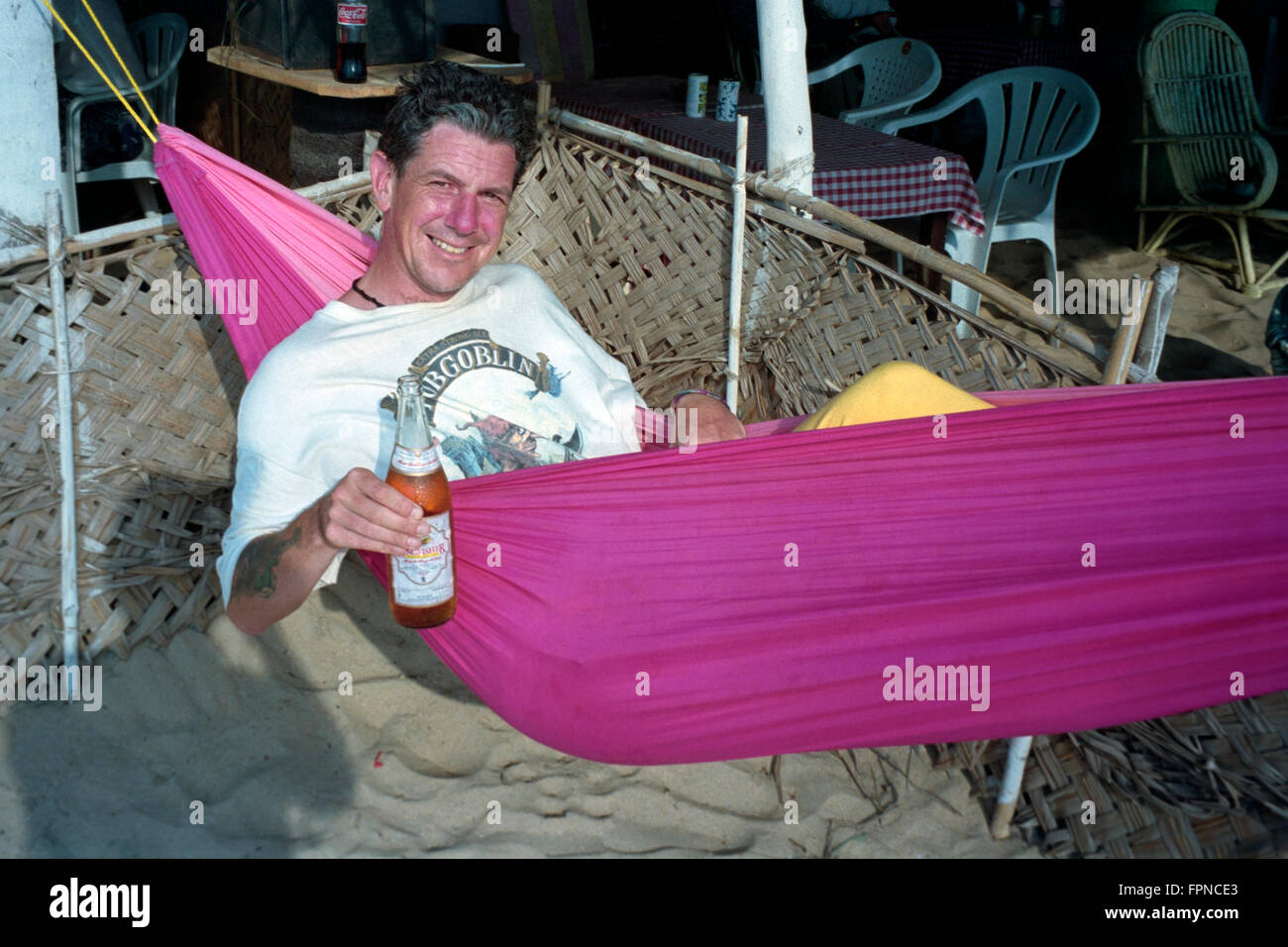 smiling male tourist in hammock with a beer bottle at a cafe in india Stock Photo