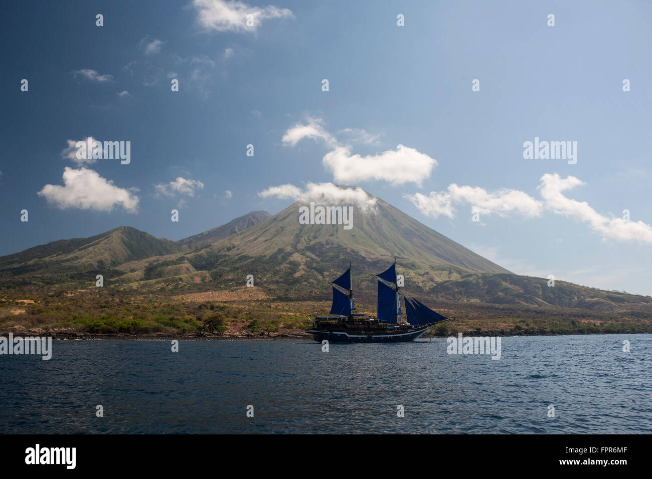 An Indonesian pinisi schooner sails near Pulau Sangeang, a remote volcanic island near Komodo in Indonesia. Stock Photo