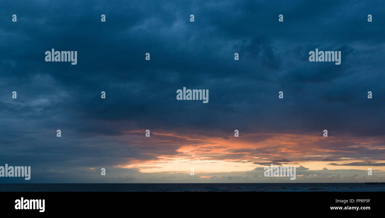 the sun sits down over the sea drawing silhouettes ashore Stock Photo