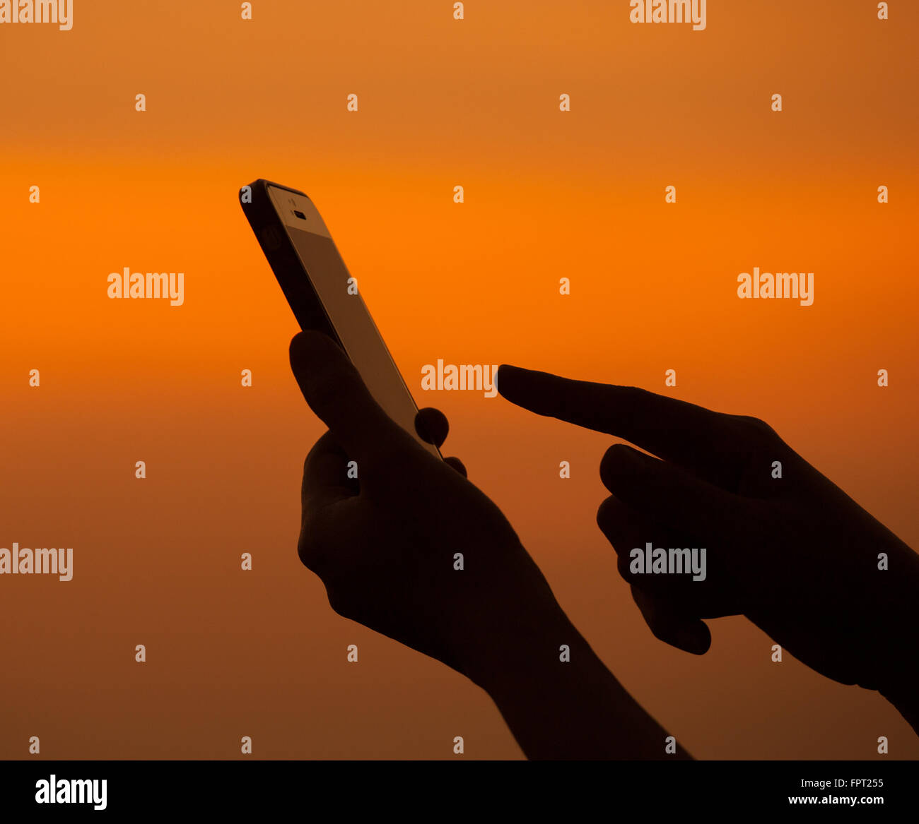 Silhouette of hand using mobile device at sunset Stock Photo