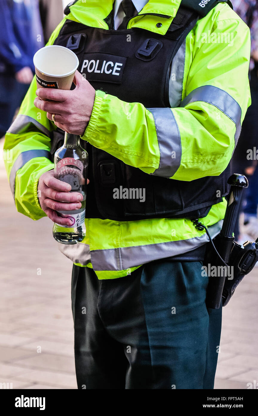 Belfast, Northern Ireland. 17 Mar 2016 - PSNI police officer carries a bottle of vodka and a cup as he disposes of alcohol confiscated from youths. Stock Photo