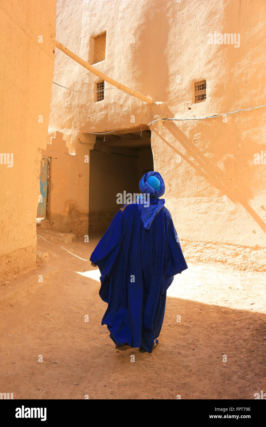 Berber man dressed in traditional Tuareg blue clothing walks through the narrow streest of a ksar in Rissani, Morocco Stock Photo