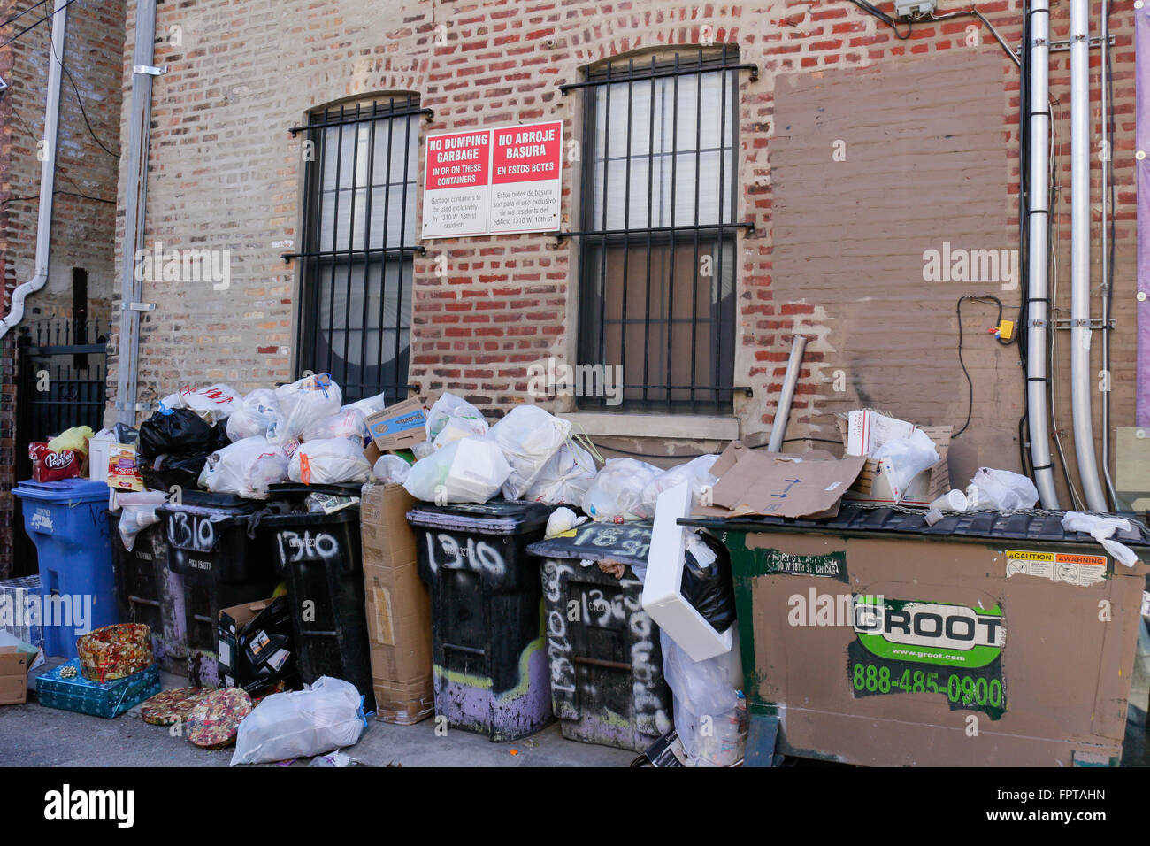 Trash piled on top of dumpsters in spite of bilingual English & Spanish signs. Pilsen neighborhood, Chicago, Illinois. Stock Photo