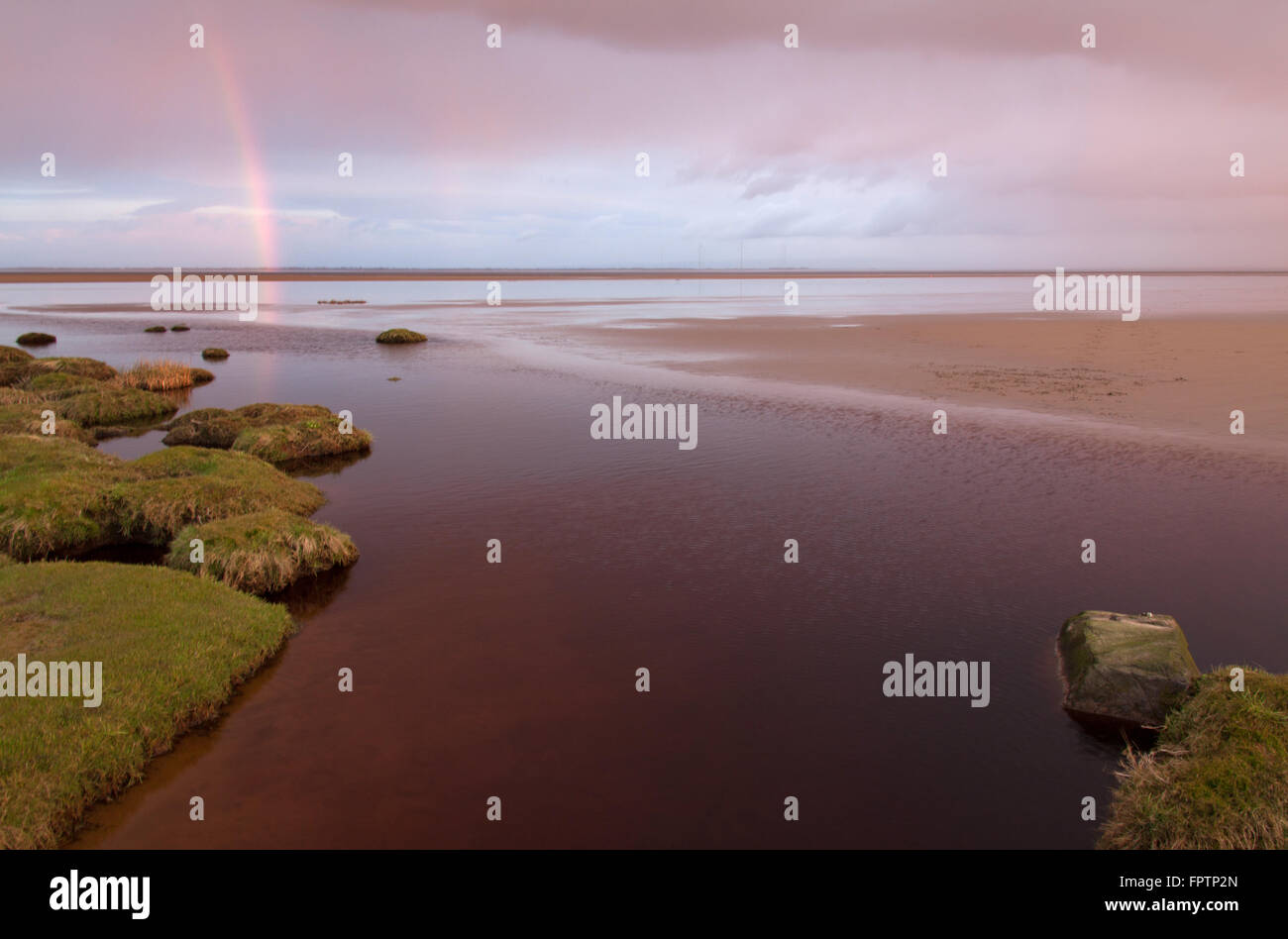 Solway Firth, Scotland. A rainbow at sunset on the Solway Firth saltmarsh and beach, near the village of Powfoot. Stock Photo