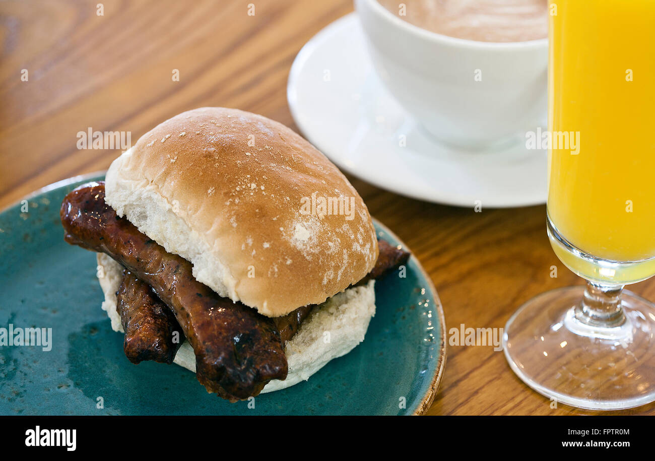 Close up selective focus image of a bread roll & sausage with coffee and orange juice Stock Photo
