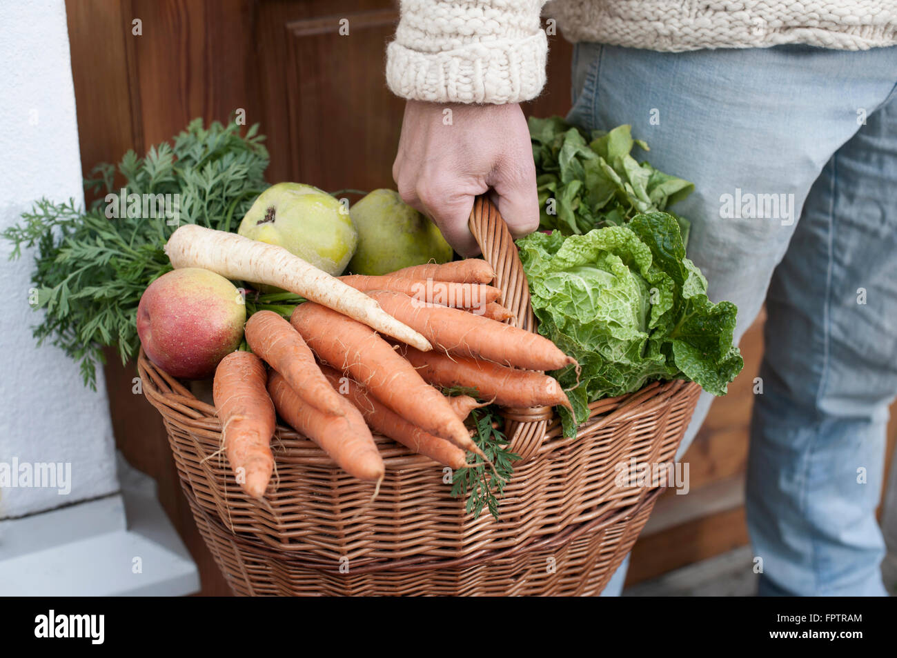 Mid section of a man holding basket full of vegetables in his hand standing in front of wholefood shop, Bavaria, Germany Stock Photo