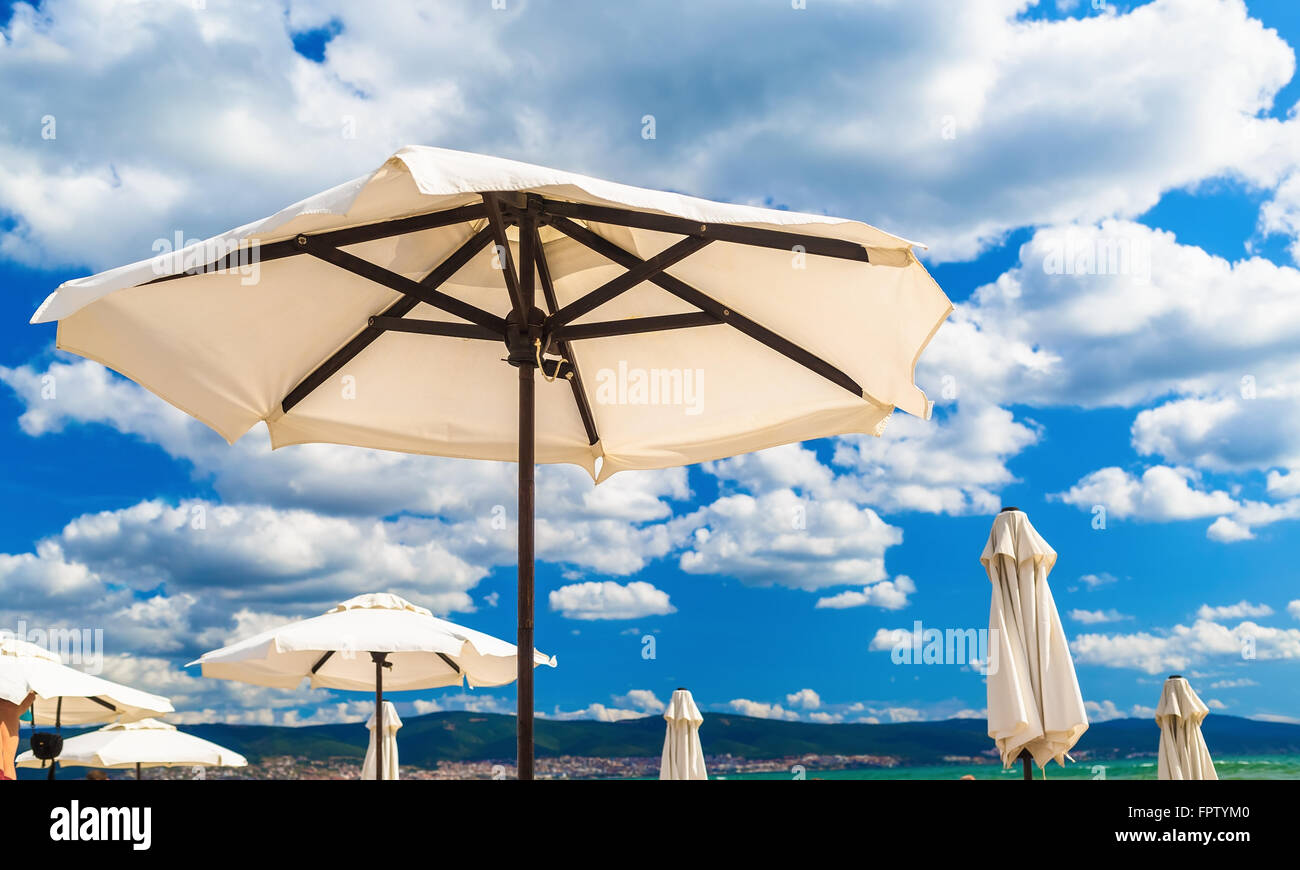 Big white parasols on a background of bright blue sky with cumulus clouds.  Beach umbrellas. Shallow depth of field. Selective fo Stock Photo - Alamy