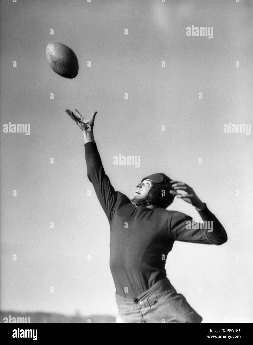 1930s FOOTBALL PLAYER REACHING UP ABOUT TO CATCH BALL Stock Photo