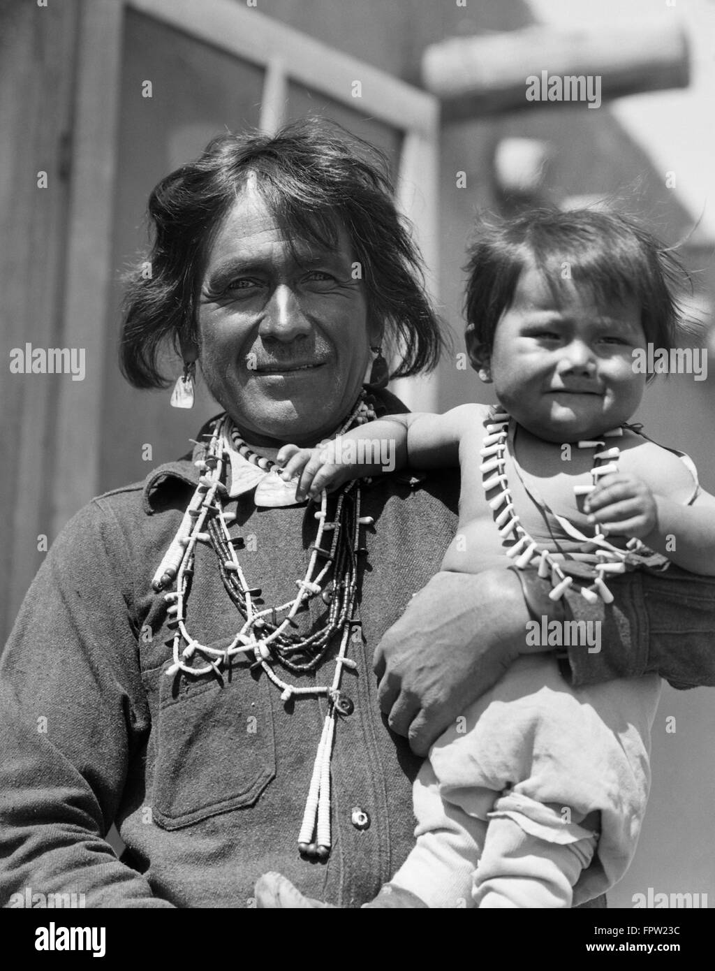 1930s SMILING NATIVE AMERICAN MAN LOOKING AT CAMERA HOLDING HIS SON COCHITI PUEBLO NEW MEXICO USA Stock Photo