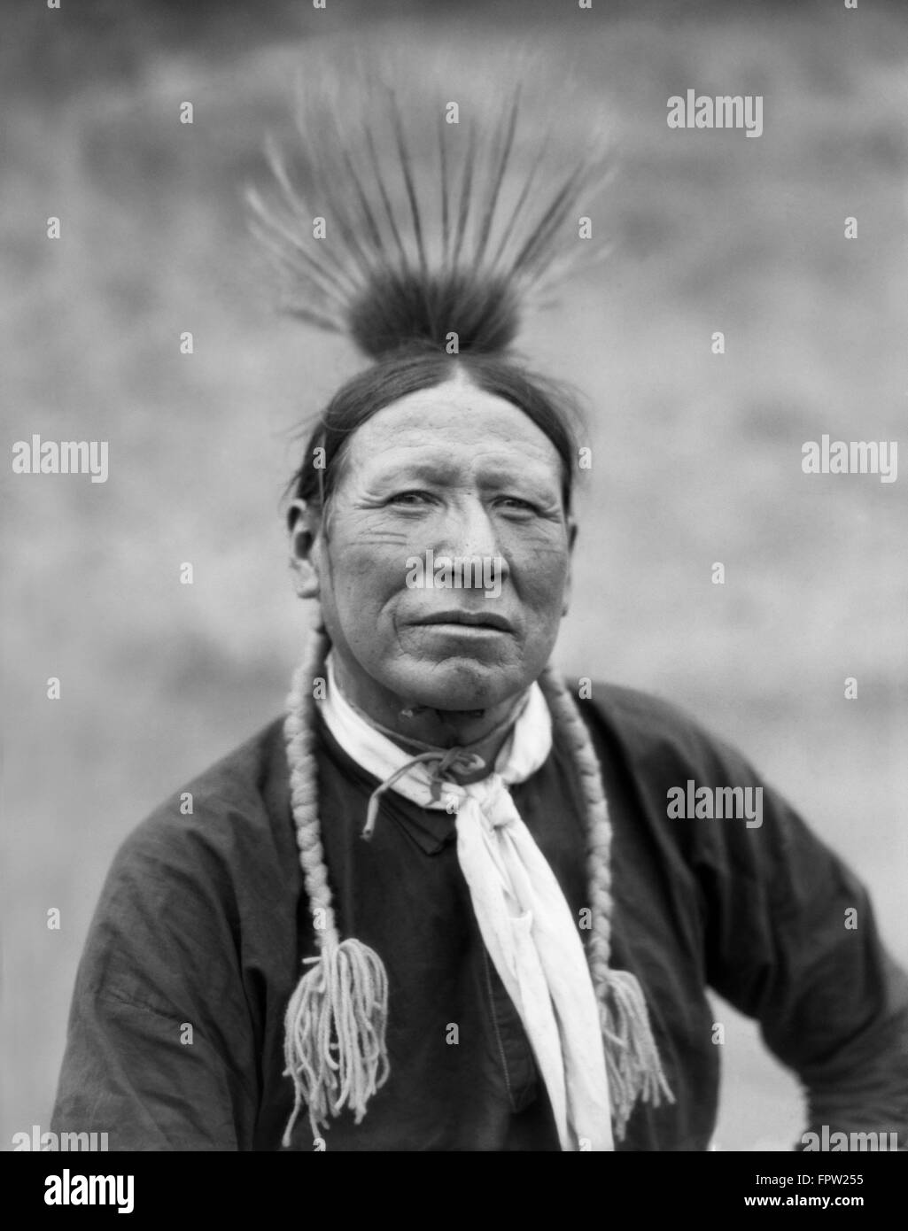 1920s PORTRAIT HANDSOME NATIVE AMERICAN INDIAN MAN OF KOOTENAY TRIBE WEARING FEATHERS AND BRAIDS LOOKING AT CAMERA Stock Photo