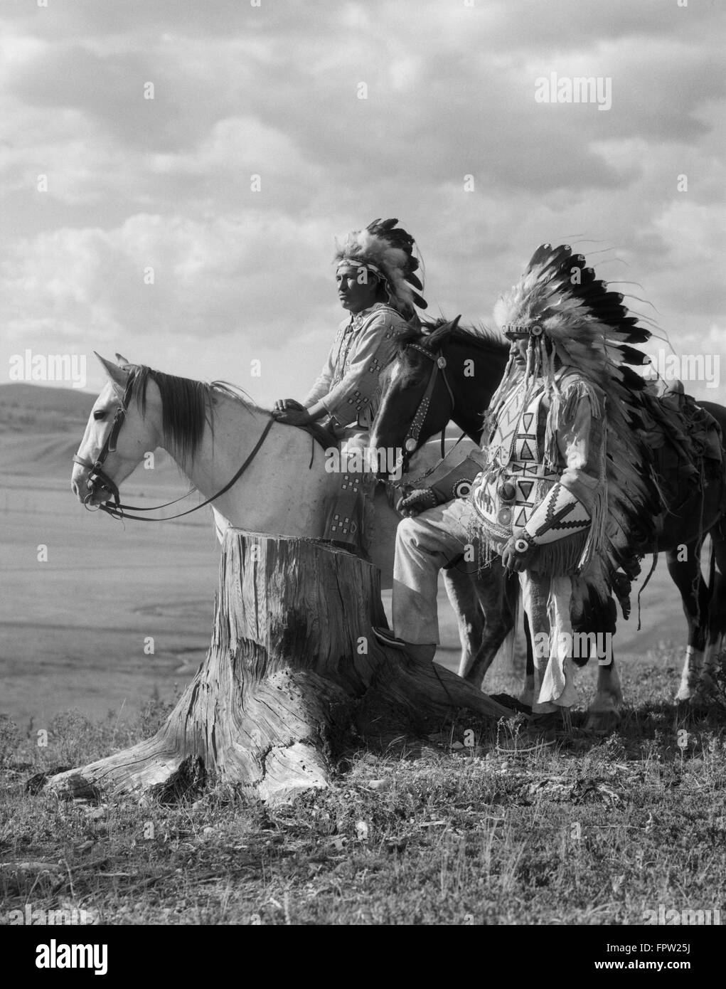 1920s TWO NATIVE AMERICAN STONEY SIOUX INDIAN MEN IN FULL FEATHER WAR BONNETS STANDING WITH HORSES ALBERTA CANADA Stock Photo