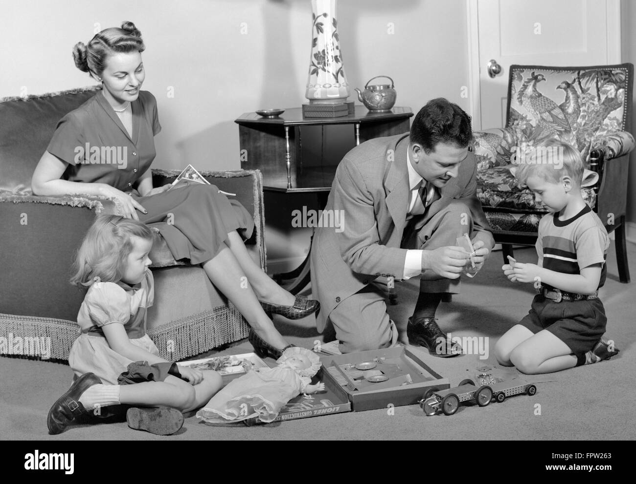 1940s FAMILY FATHER MOTHER DAUGHTER SON TOGETHER IN LIVING ROOM WITH TOY ERECTOR SET Stock Photo