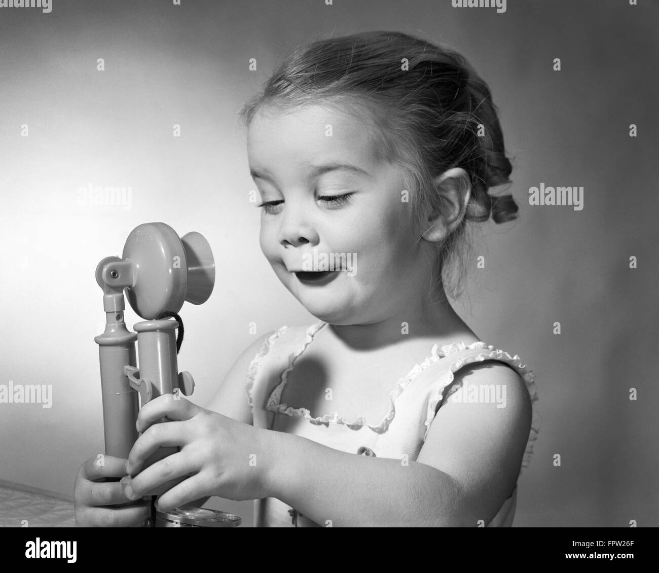 1960s GIRL BOTH HANDS HOLDING A  TOY CANDLE STICK PHONE FUNNY FACIAL EXPRESSION Stock Photo