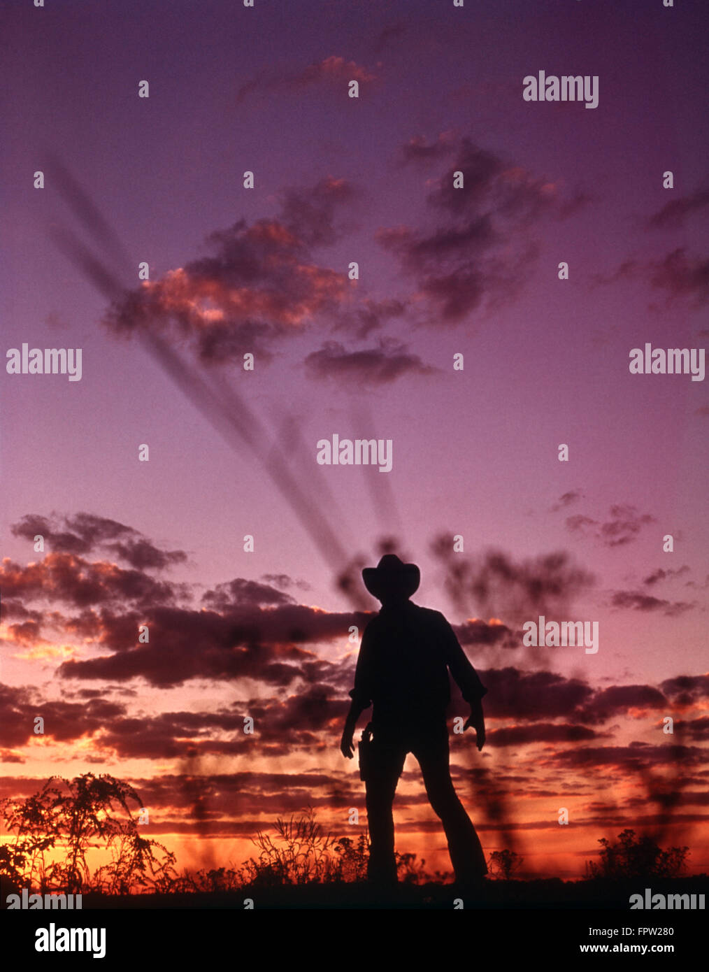 ANONYMOUS COWBOY GUNFIGHTER SILHOUETTED AT DUSK BY SUNSET SKY Stock Photo