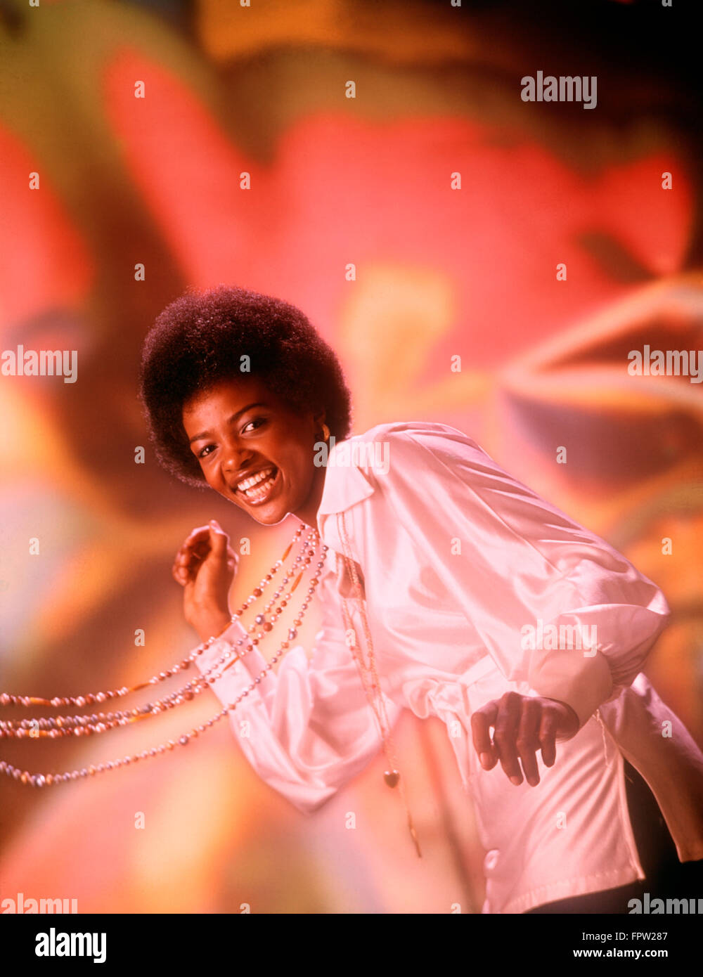 1970s LAUGHING YOUNG AFRICAN AMERICAN WOMAN AFRO HAIR STYLE WHITE SILK SHIRT SINGING DANCING BEADS SWINGING LOOKING AT CAMERA Stock Photo