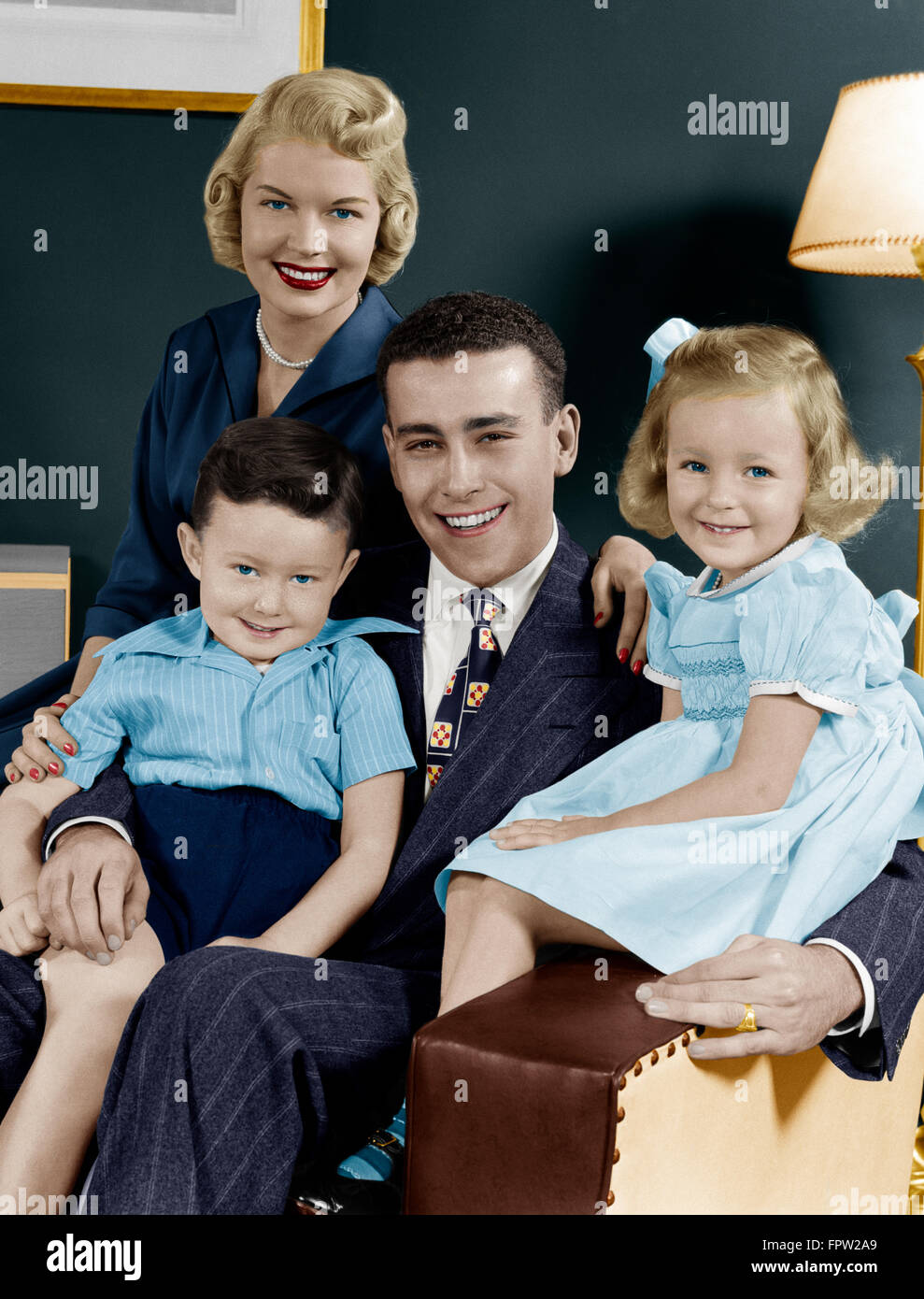 1940s 1950s FAMILY OF FOUR PORTRAIT SITTING IN LIVING ROOM CHAIR LOOKING AT CAMERA Stock Photo