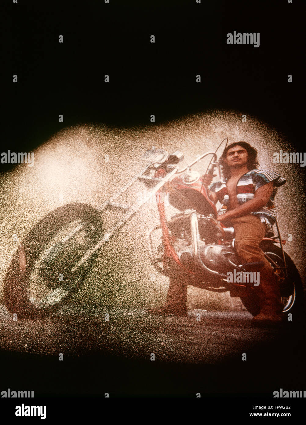 1970s HISPANIC HIPPIE SYTLE MAN ON CHOPPER MOTORCYCLE WEARING SERAPE VEST SPECIAL VISUAL TEXTURED EFFECT Stock Photo