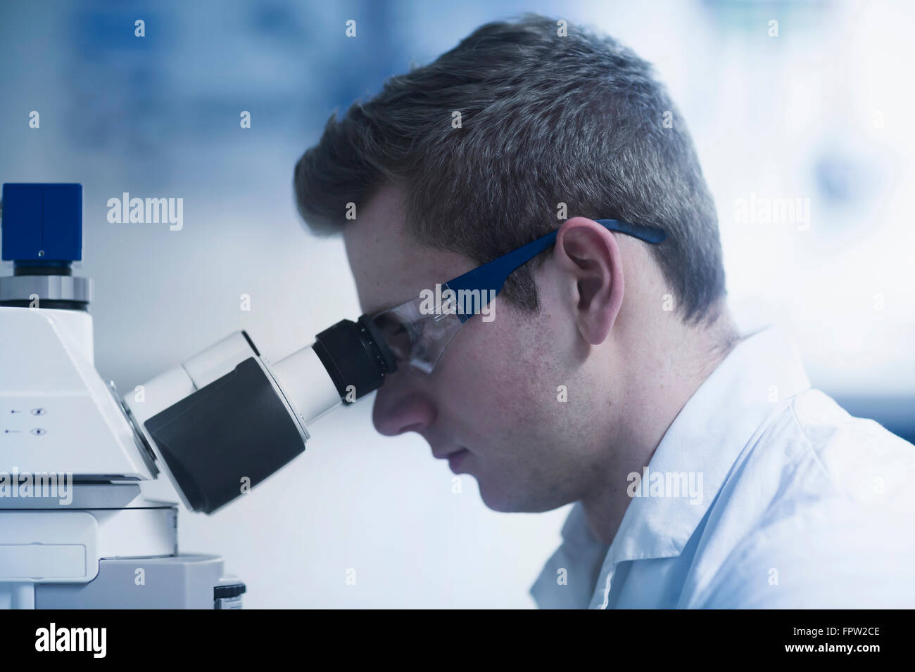 Young male scientist looking through microscope in an optical