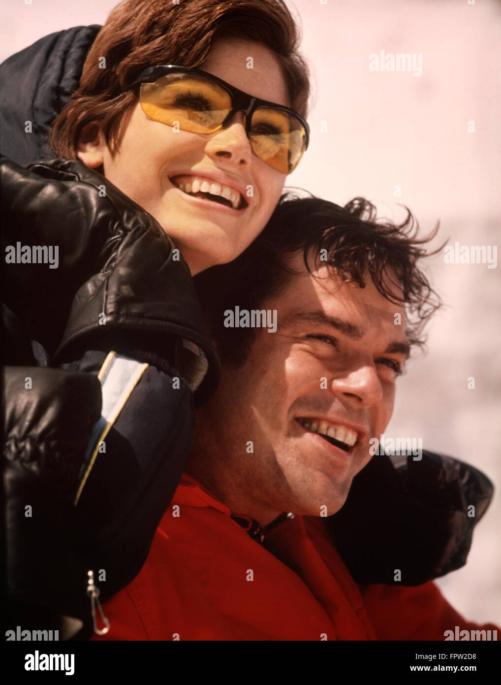 1970s SMILING HAPPY PORTRAIT MAN WOMAN SKI COUPLE JACKETS GLOVES WOMAN WEARING YELLOW GOGGLES GLASSES Stock Photo