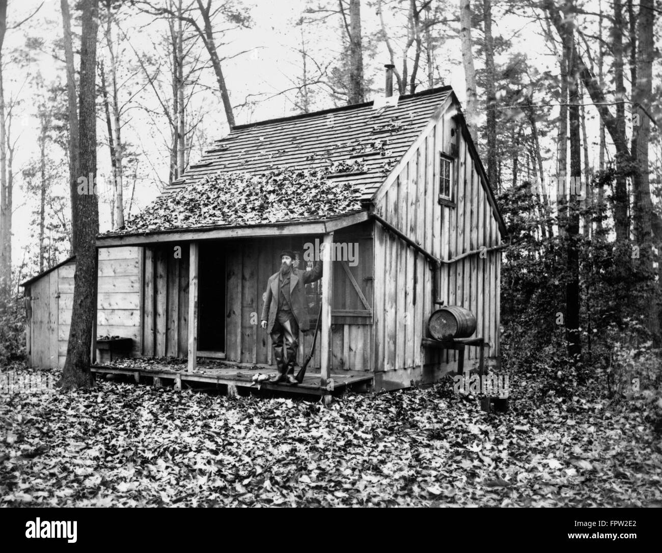 1880s HUNTER STANDING ON FRONT PORCH OF CABIN IN WOODS Stock Photo