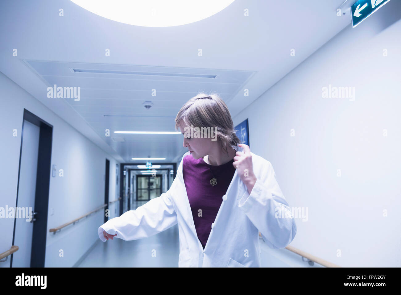 Young female doctor looking at her hand while walking in hospital corridor, Freiburg im Breisgau, Baden-Württemberg, Germany Stock Photo