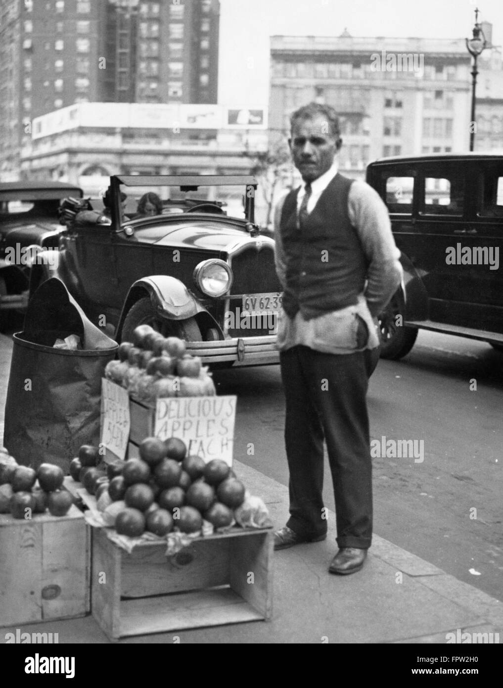 1930s SIDEWALK APPLE VENDOR MAN LOOKING AT CAMERA DURING THE GREAT DEPRESSION Stock Photo