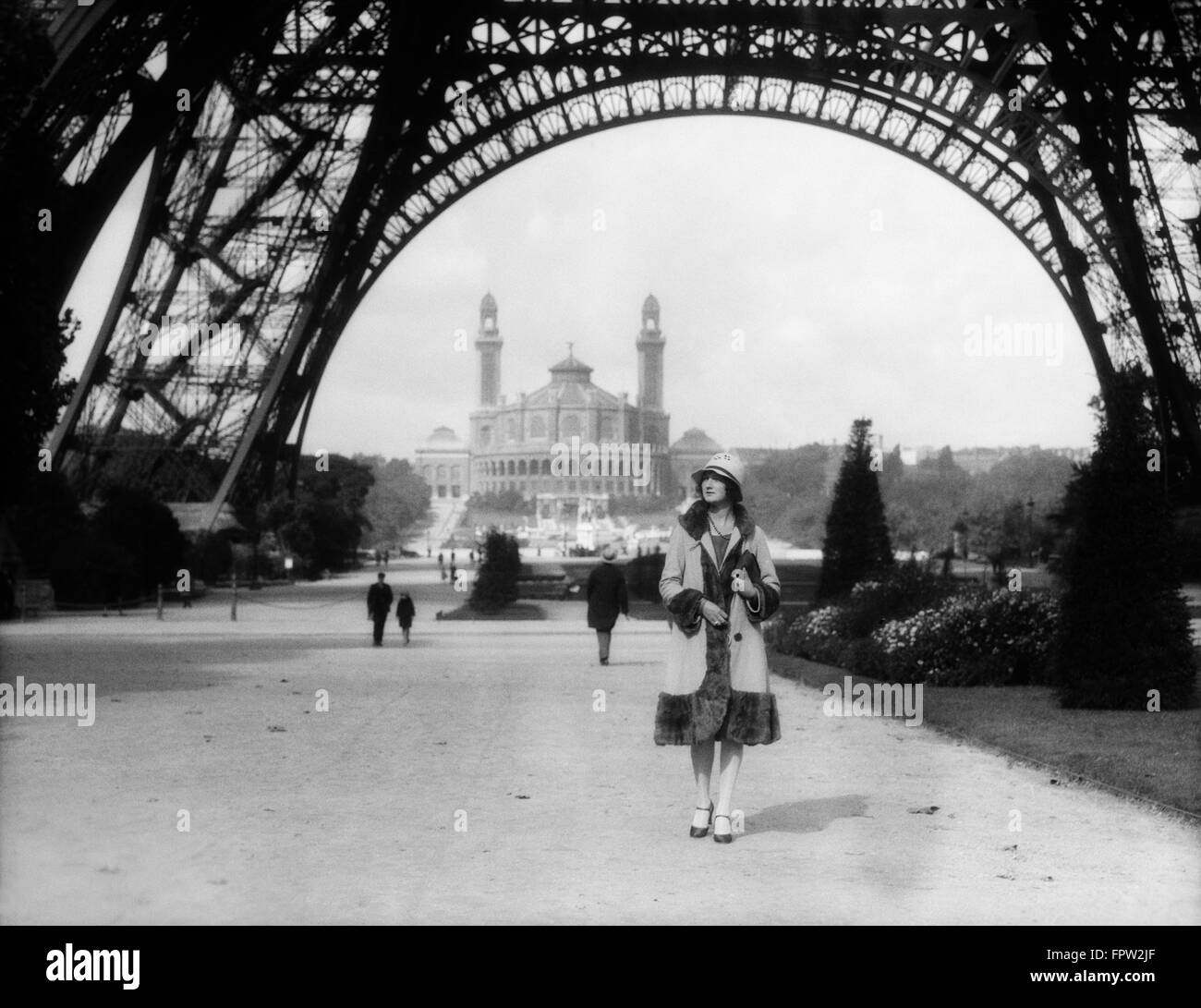 1920s WOMAN WALKING UNDER THE EIFFEL TOWER WITH THE TROCADERO IN BACKGROUND PARIS FRANCE Stock Photo