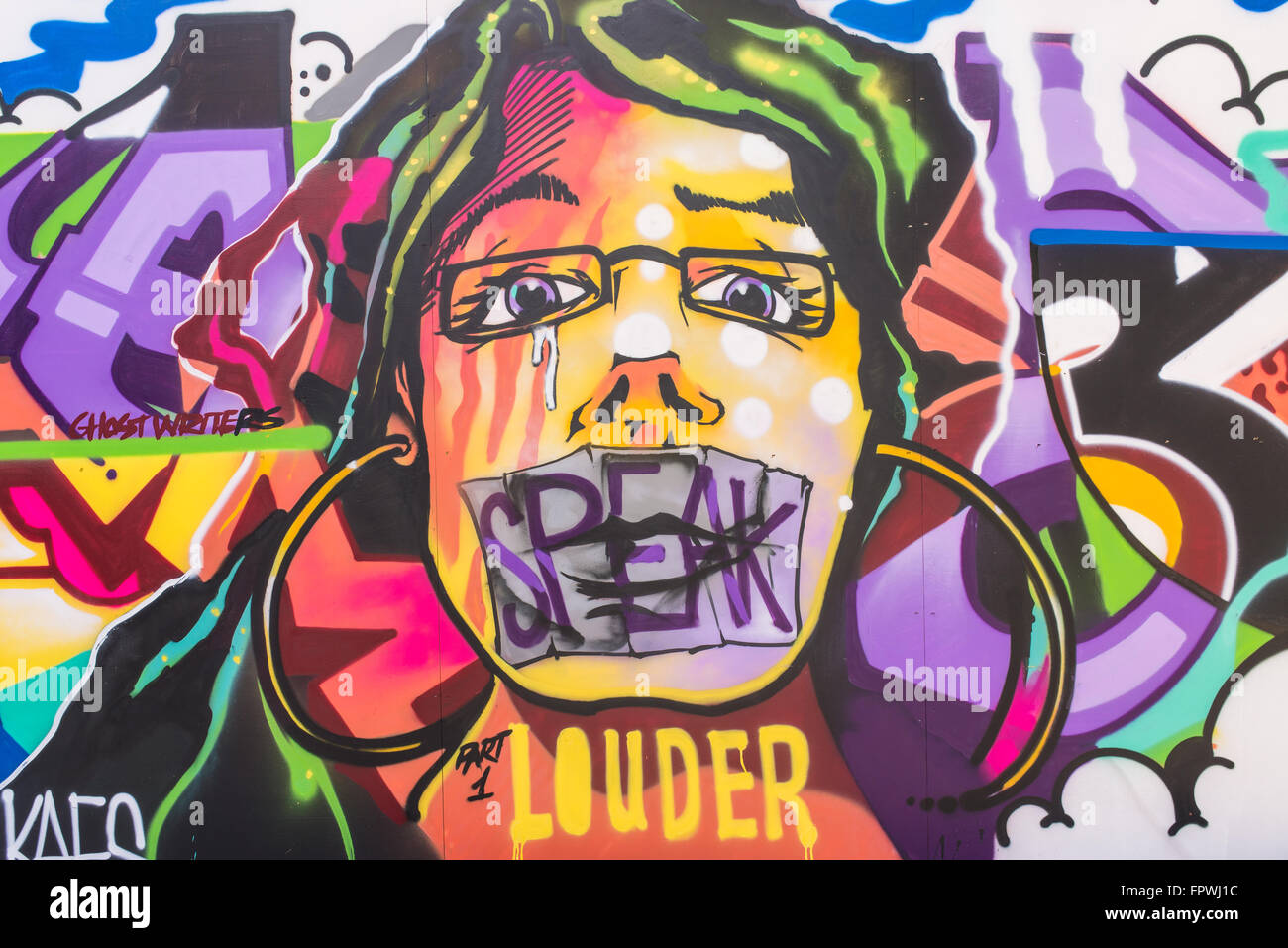 Street art mural showing a woman face with the mouth taped shut and the words 'Speak louder'. Stock Photo