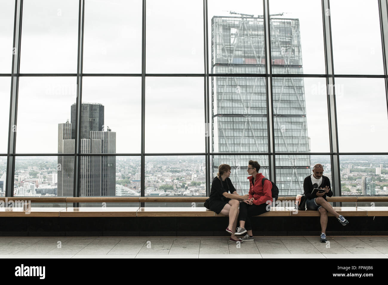 Couple holding hands and man looking at ipad sitting on the  Sky Garden rooftop garden of the Walkie Talkie, 20 Fenchurch Street, London Stock Photo