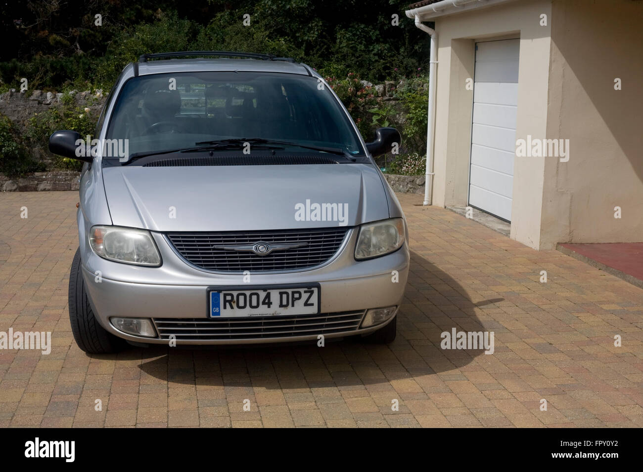 Silver Chrysler grand voyager mpv people carrier parked on block paved drive near garage Stock Photo