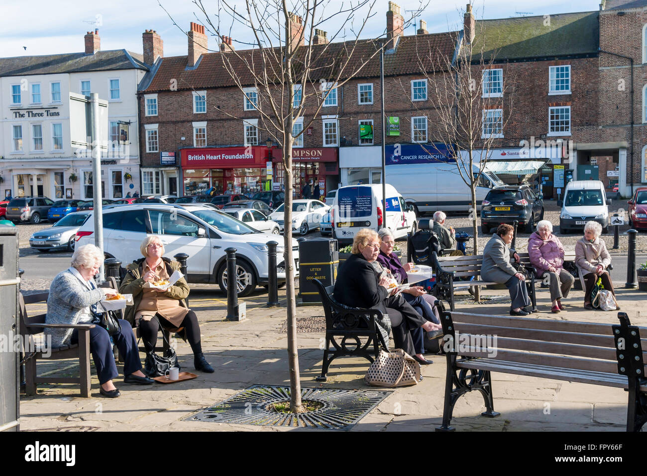 Senior people enjoying Spring Sunshine in Thirsk Market Place North Yorkshire, many eating take away fish and chips Stock Photo