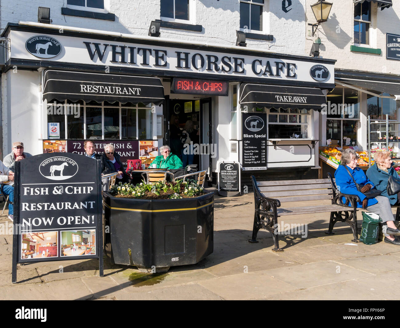 People relaxing  outside the White Horse Fish and Chip Café in Thirsk Market Place in the town centre on sunny Spring day Stock Photo
