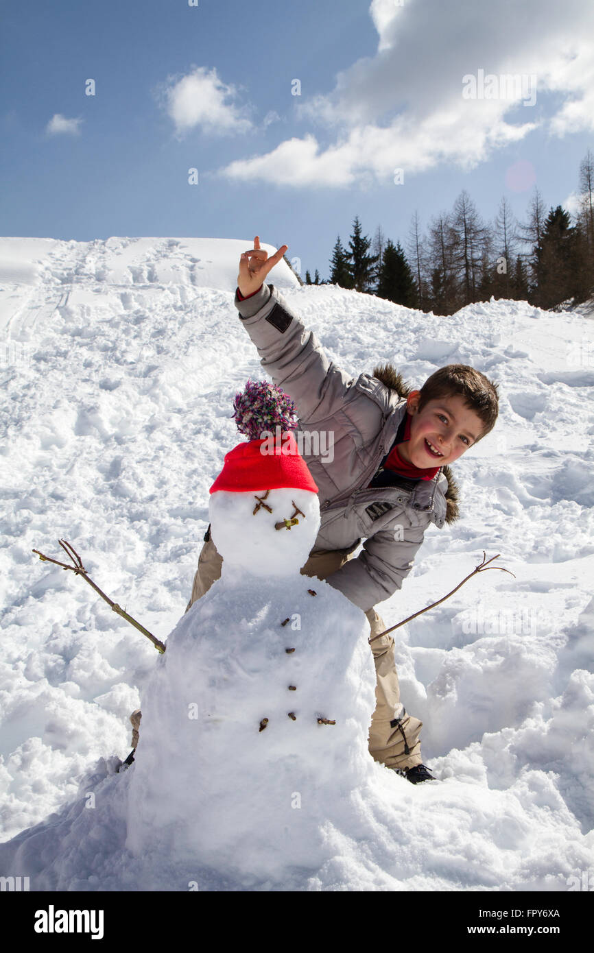 child with snowman with orange wool hat and blue sky Stock Photo