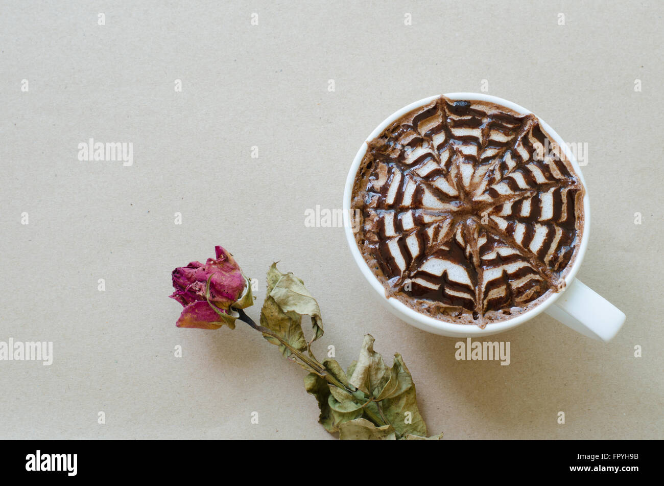 A cup of coffee with latte art and wither rose on brown paper background Stock Photo