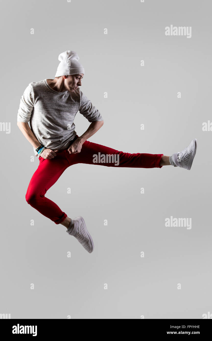 One young attractive modern style dancer guy in casual red jeans working out, dancing and jumping in mid-air. Full length photo Stock Photo