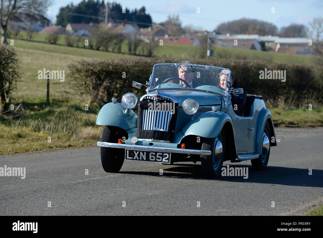 Eaglesham,  East Renfrewshire, Scotland, UK. 20th March, 2016. Fine weather in the Glasgow area allowed this couple the enjoyment of having the roof down on their Singer Roadster 4AB classic car. Stock Photo