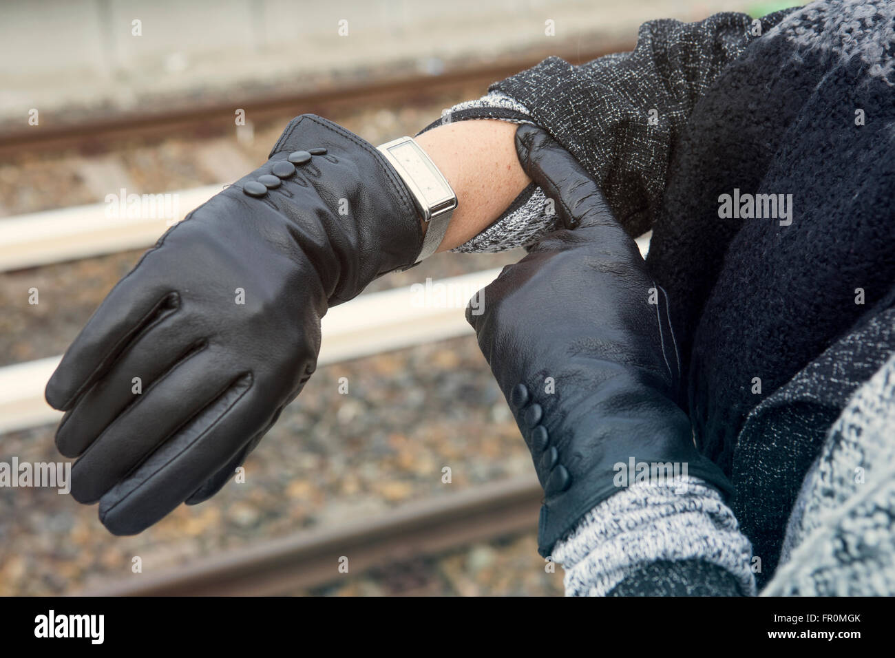 close-up of woman wearing gloves looking at her watch at train station Stock Photo