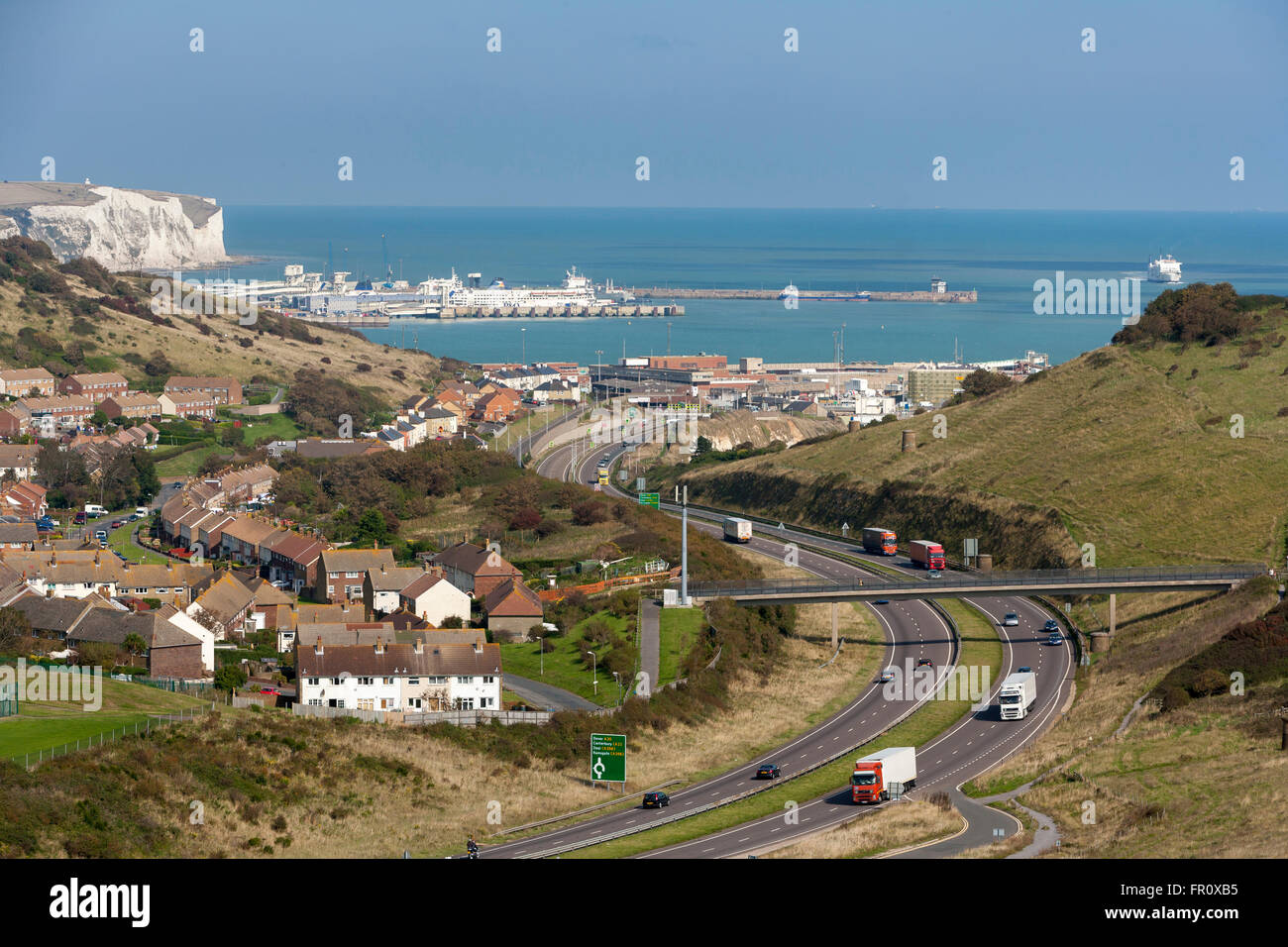 Distant view of Dover harbour and white cliffs with A20 road and trucks in foreground Kent Stock Photo