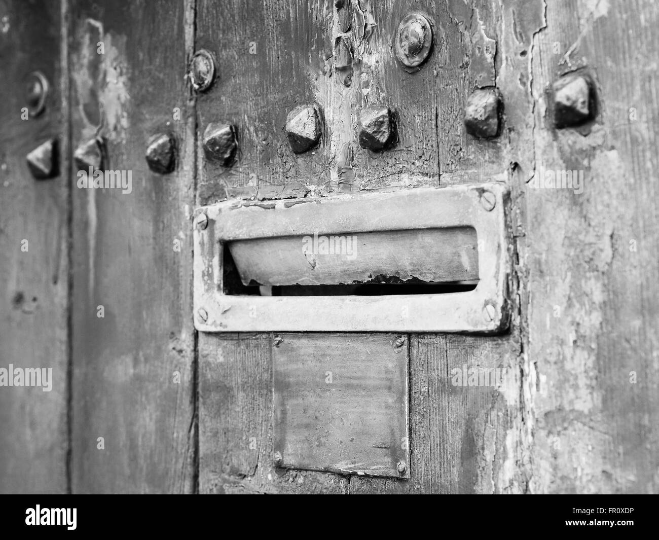 Ancient rusty iron letterbox opened on wooden door with metal ornaments, black and white conversion, intentionally blurred. Stock Photo