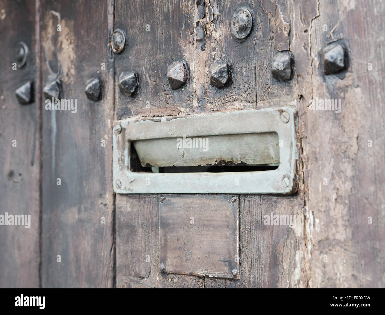 Ancient rusty iron letterbox opened on brown wooden door with metal ornaments, intentionally blurred. Stock Photo