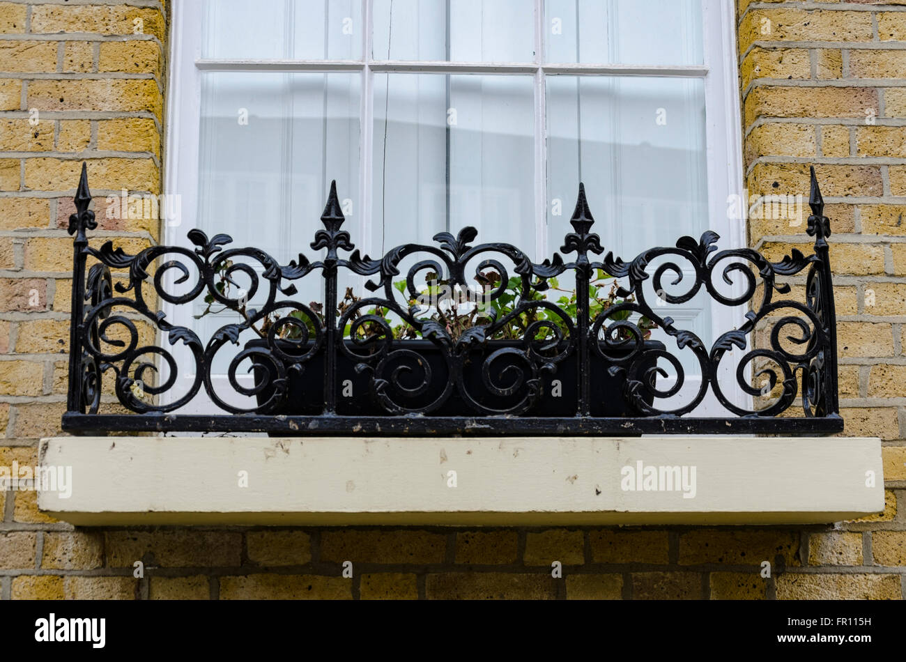 An ornate window ledge with iron railings and a flower box. Stock Photo